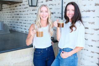 Two women holding drinks against a brick wall.